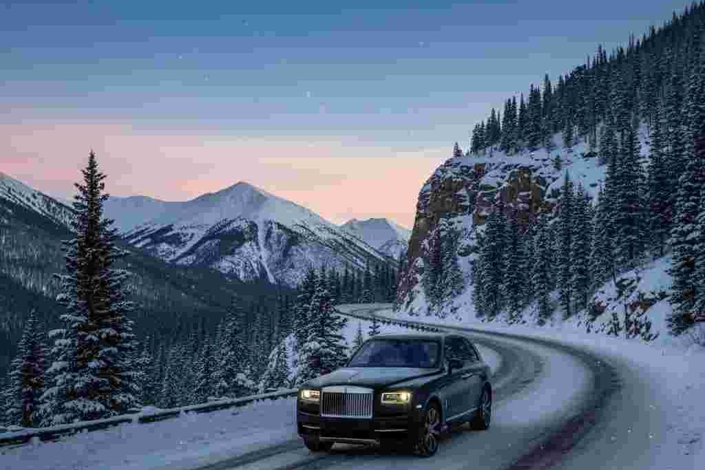 Luxury vehicle on mountain road in Colorado with snow-lined trees and twilight sky